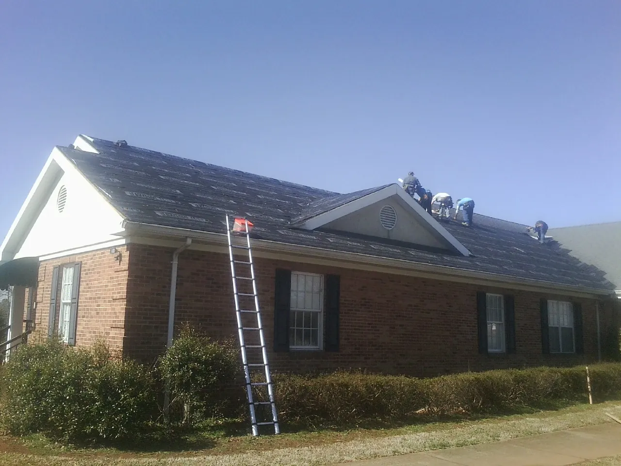 Crew tearing shingles off a brick ranch roof with a ladder set — Metal Roof Repair work by our crew in Apple River