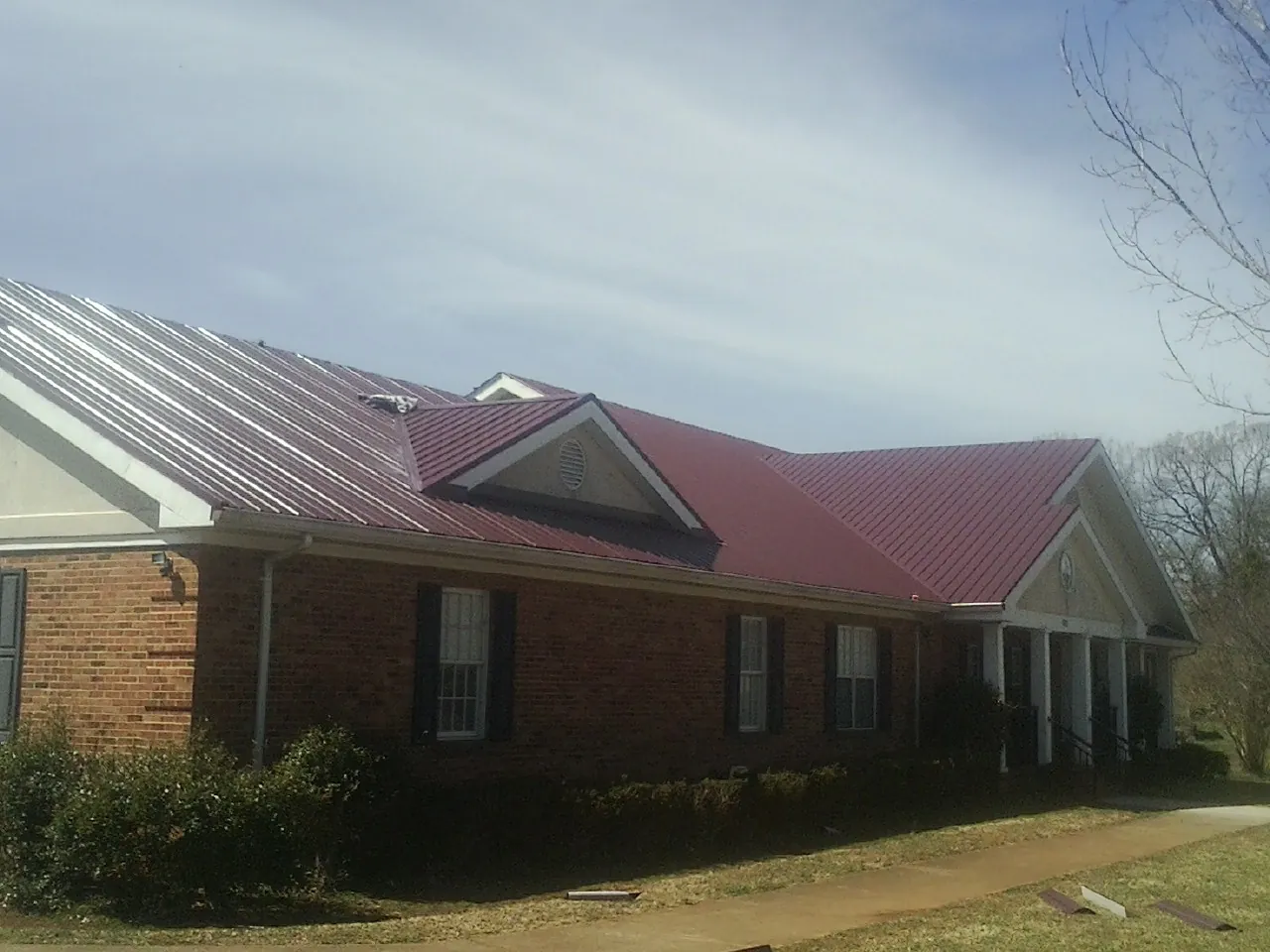Red metal roof with gabled entries on a long brick building, from a Hail Damage Roof Repair job in Apple River