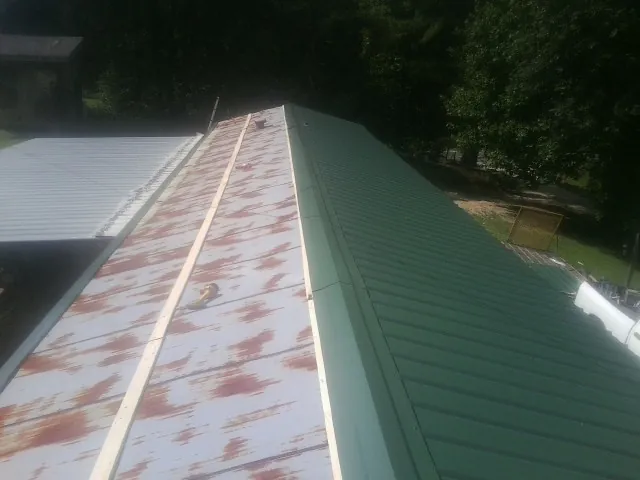 Old rusted panels beside newly installed green metal roofing — Wind Damage Roof Repair by Roofing Brothers in Apple River