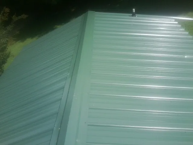 New green metal panels meeting at the ridge of a roof — Flat Roof Repair work by our crew in Apple River