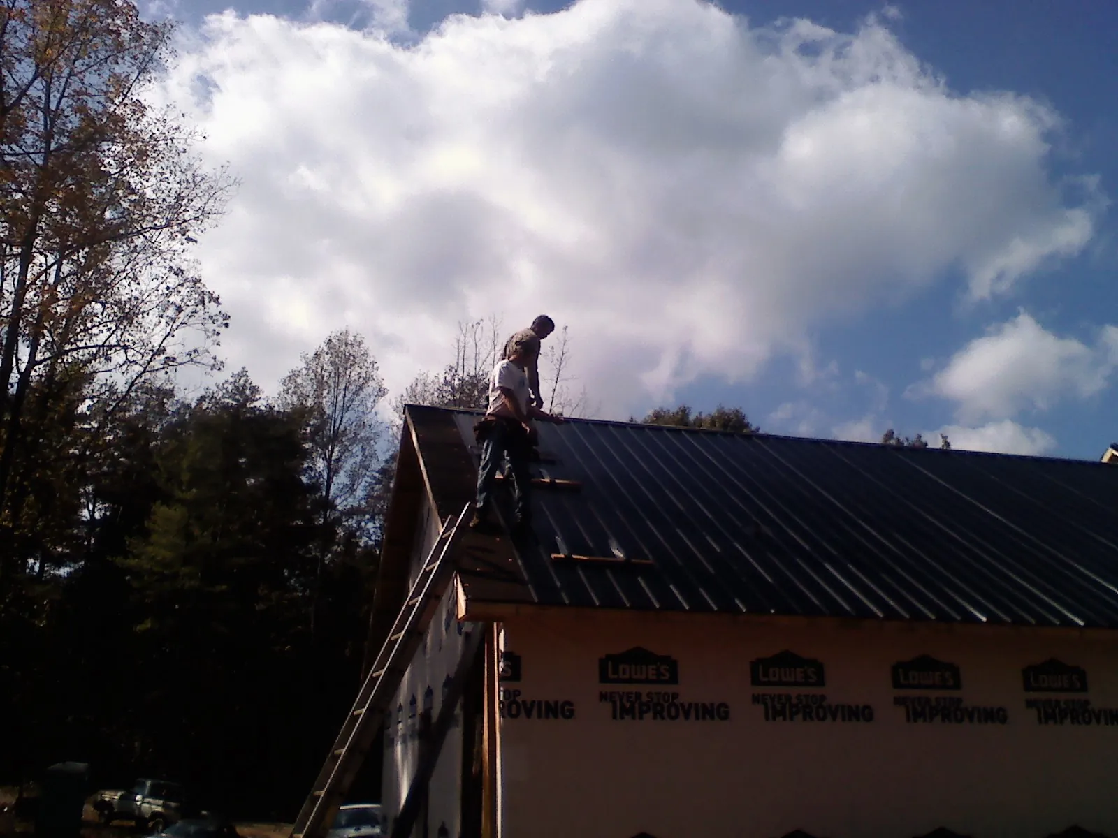 Roofer fastening dark metal panels high against a cloudy sky, from a Roof Inspection job in Apple River