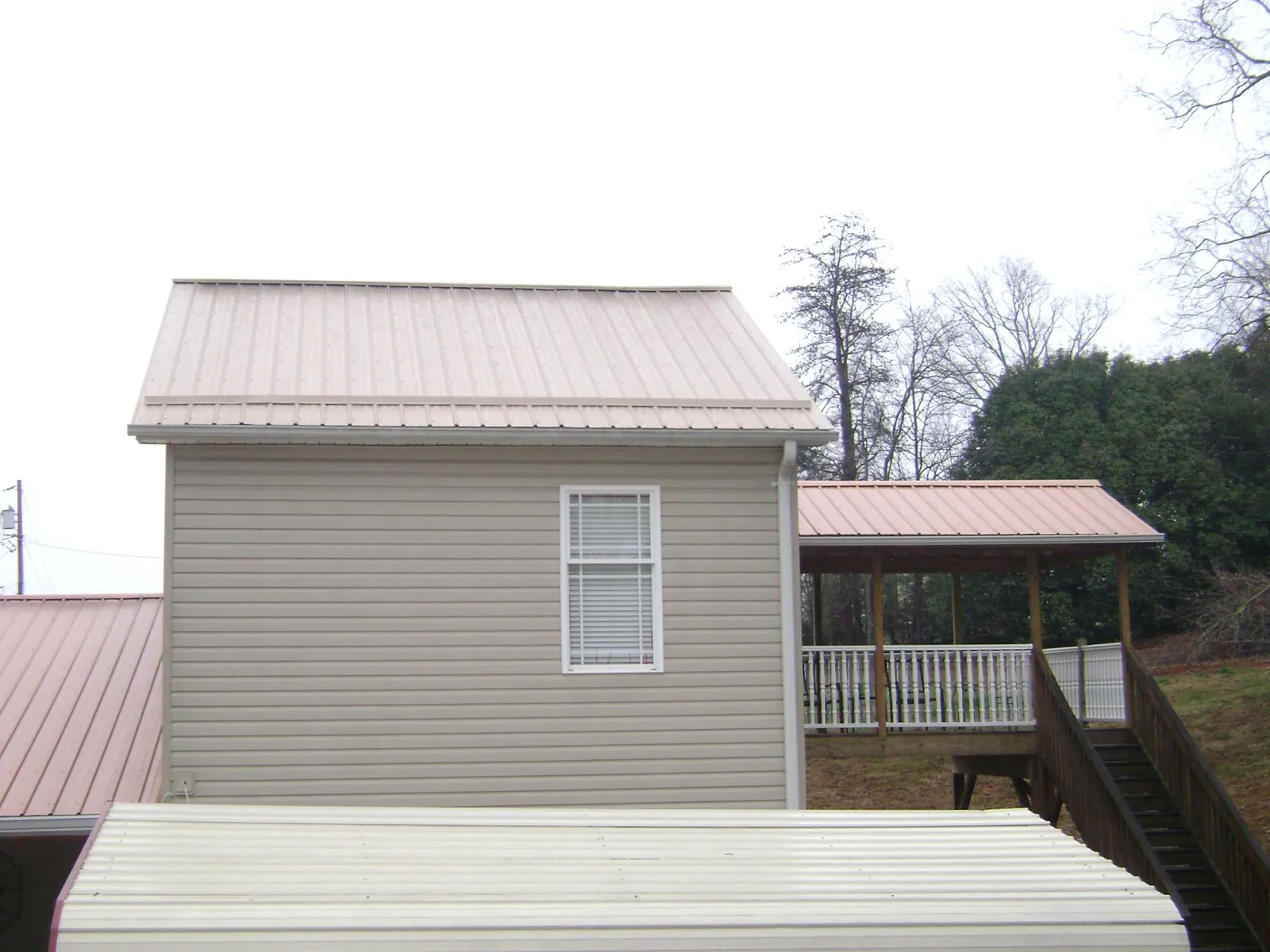 Tan metal roofs on a two story addition and attached porch, from a Roof Replacement job in Apple River